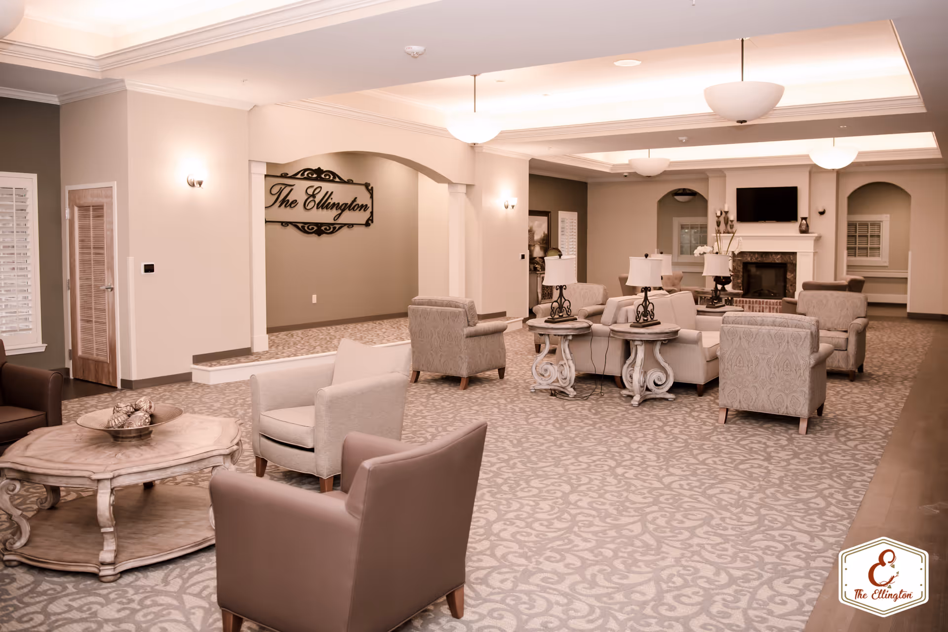 Spacious senior living lounge with multiple armchairs, side tables, a fireplace, and a wall sign reading "The Ellington".