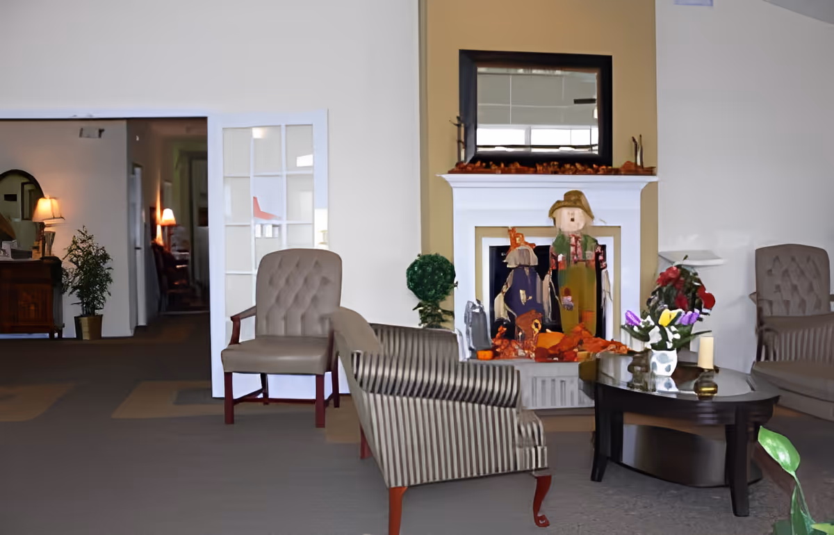 Seating area in a senior living room with armchairs around a coffee table and a decorated fireplace.