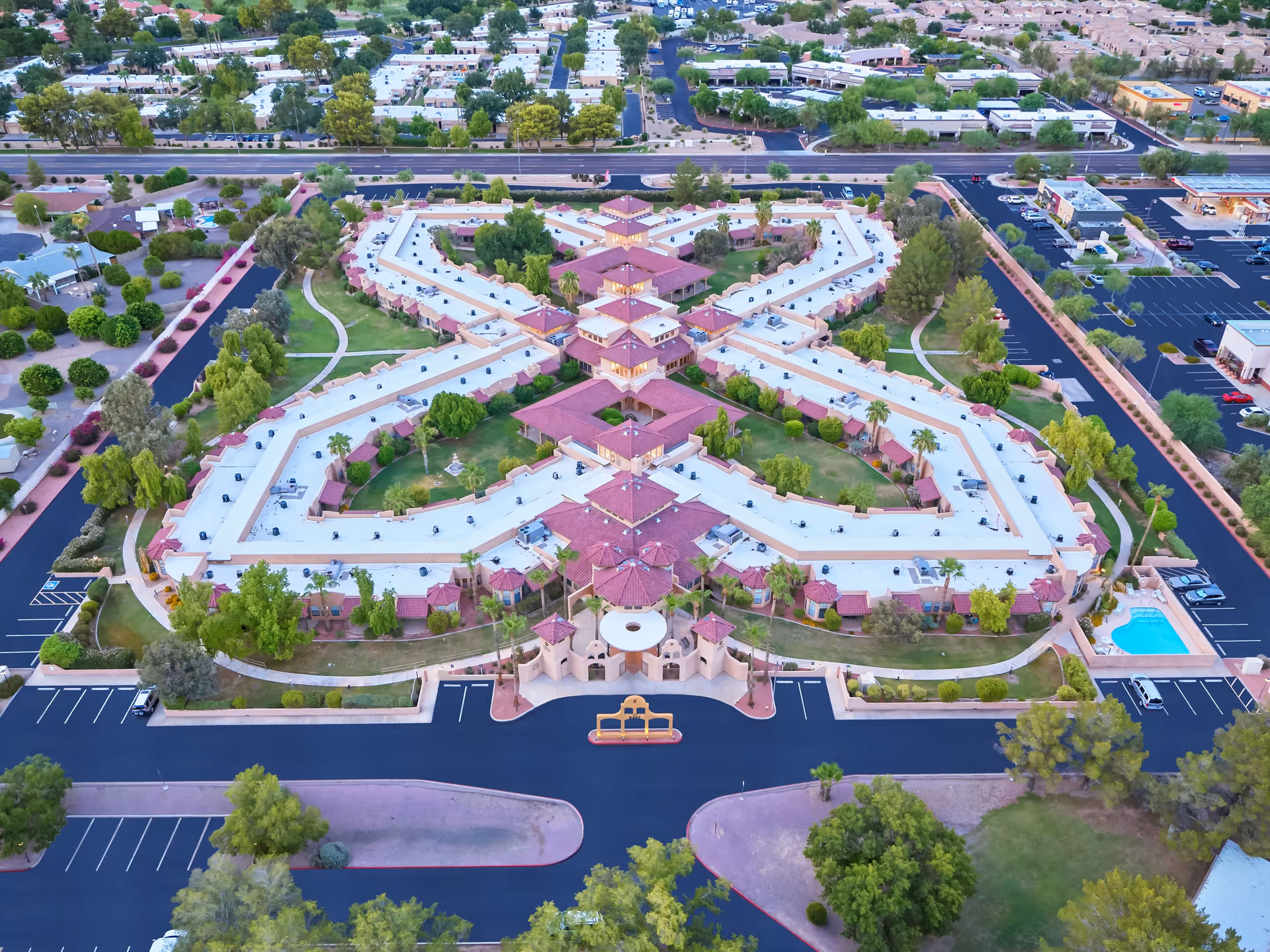 Aerial view of a star-shaped senior living complex with connected single-story buildings, landscaped courtyards, parking areas and a swimming pool.