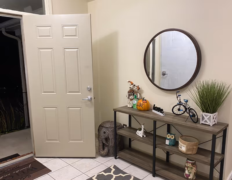 Entryway with an open front door, a console table topped with decorative items and a round wall mirror.