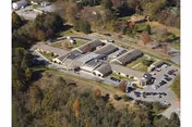Aerial view of a large single-story healthcare facility surrounded by trees and greenery, with multiple parking areas and several connected buildings forming a campus-like layout.