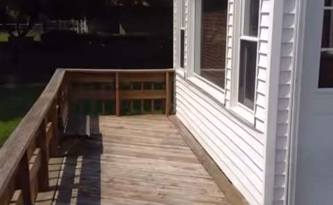 Wooden outdoor porch with railing beside white-siding building.