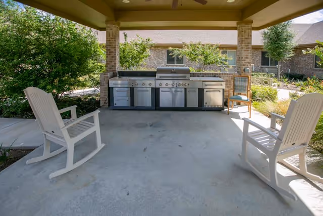 Covered outdoor patio with a stainless steel grill station and two white rocking chairs.