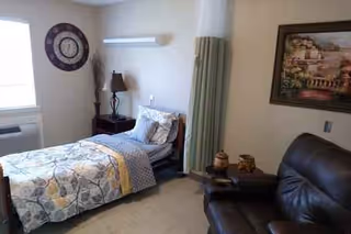 A furnished senior living bedroom with bed, nightstand, lamp, and wall art.