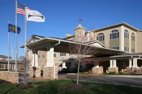 Exterior view of a senior living facility entrance with flags and a covered driveway.