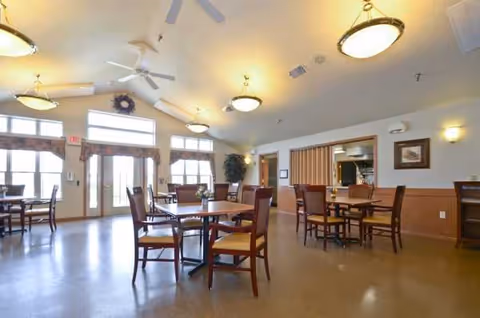 A dining room with round tables and chairs in a senior living facility.