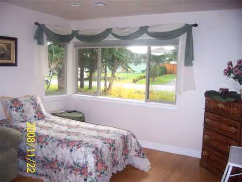 Bedroom in a senior living facility with floral quilt, window, and dresser.