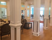 Bright interior common lounge with white columns, seating, and dining tables visible in the background.