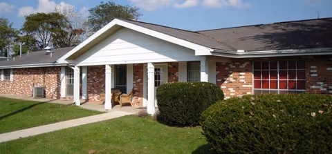Front view of a brick senior care center entrance with columns and well-kept shrubs.