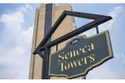 A hanging sign that reads "Seneca Towers" and the number 200 in front of a tall residential tower against a partly cloudy sky.