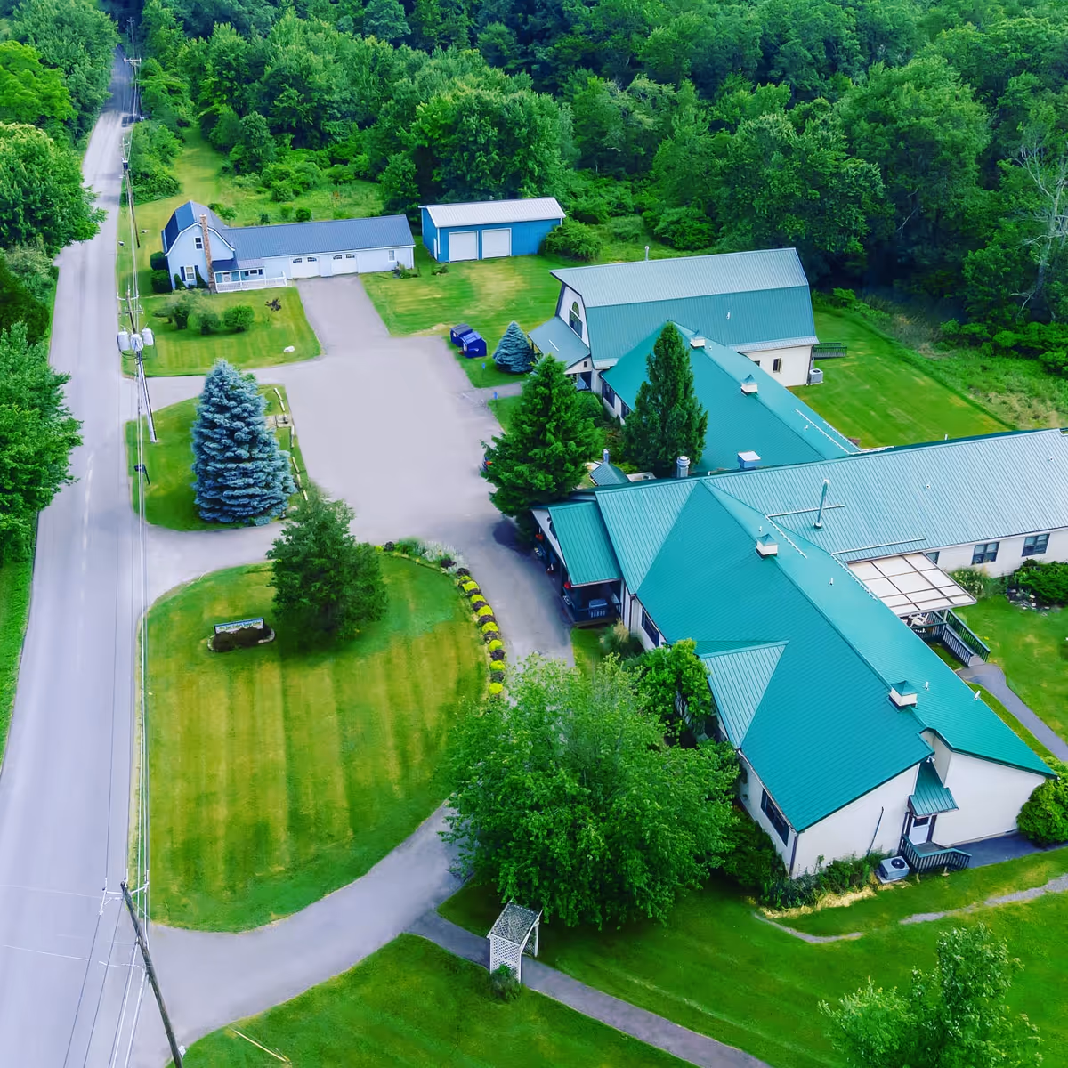 Aerial view of a senior living campus with green-roofed buildings, manicured lawns, driveways and surrounding trees.