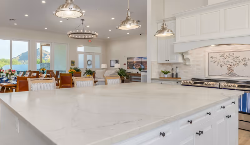 Spacious open-plan kitchen with a large marble island, pendant lights, dining table and seating, and windows showing a mountain view.