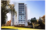 Multi-story residential building on a grassy lawn with trees under a clear blue sky.