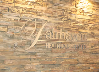 Stone wall with the words 'Fairhaven Healthcare Center' mounted on it in elegant lettering, illuminated by overhead lights.