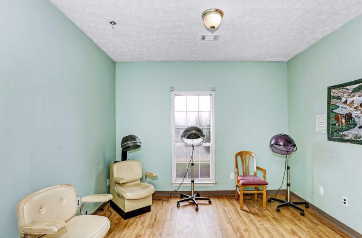Small salon room with three vintage hooded hair dryers, seating, and a window on mint green walls.