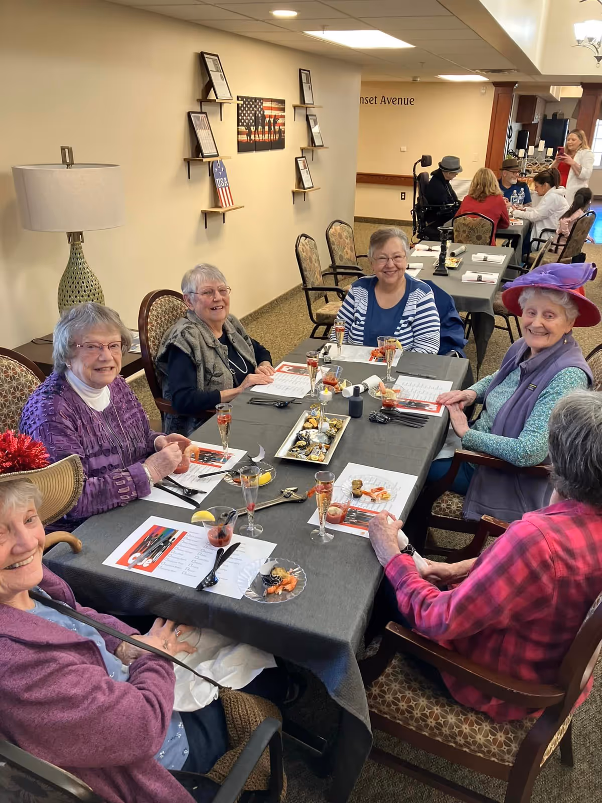 Several elderly women smiling and seated around a decorated dining table in a retirement community dining room.