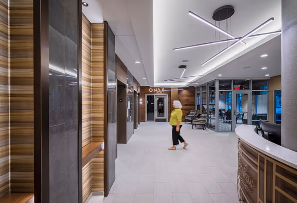 Modern lobby interior with a curved reception desk, seating area, and a person walking toward glass doors.