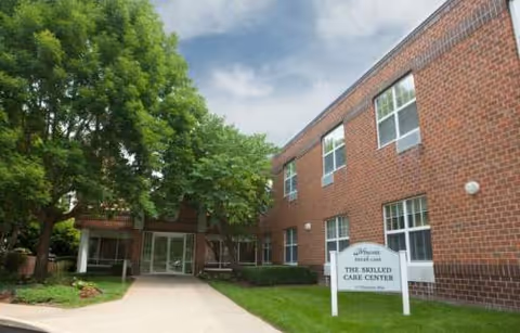 Brick senior living building exterior with welcoming entrance and Wingate sign beside a green lawn.