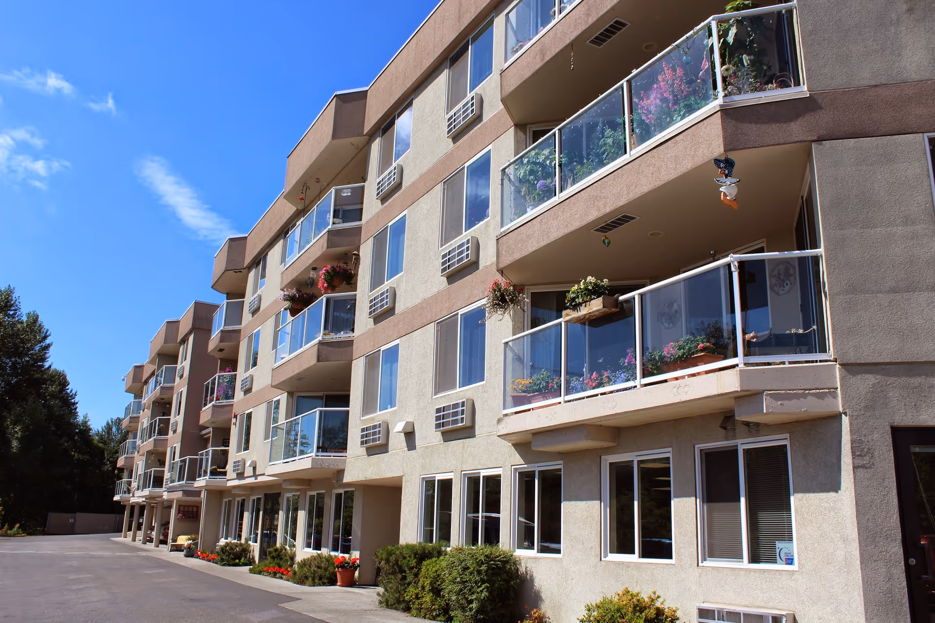Exterior view of a multi-story residential building with balconies decorated with flowers and plants under a clear blue sky.