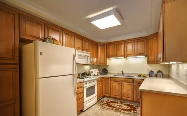 Well-lit kitchen with wooden cabinets, a white refrigerator and stove, sink, and countertop workspace.