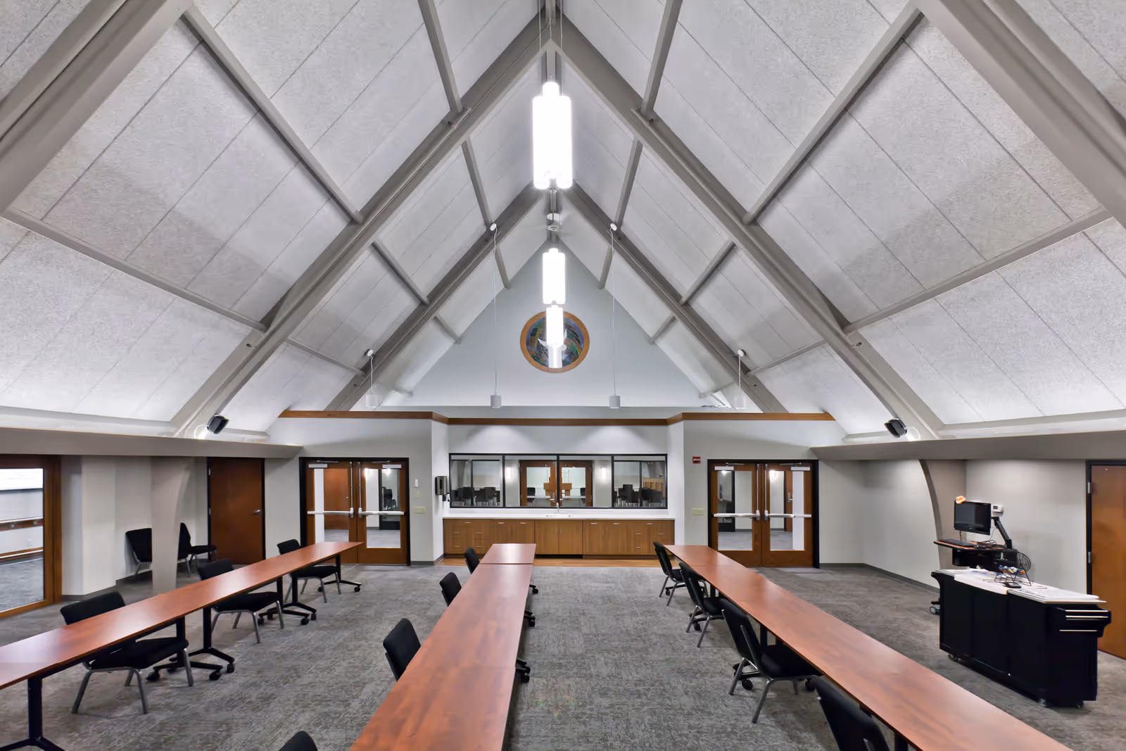 Spacious interior of a meeting room with long tables and a high vaulted ceiling.