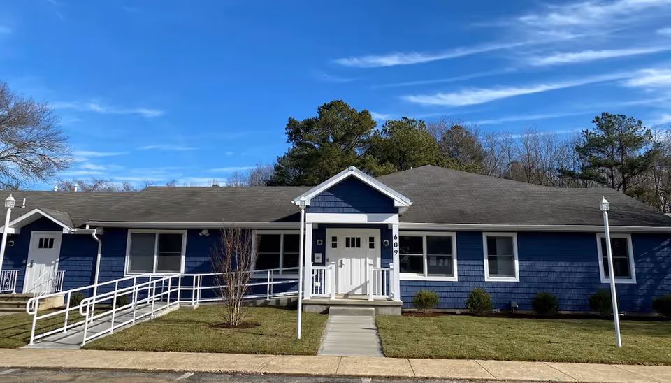 Blue single-story building with white trim, central entrance, and wheelchair ramp under a blue sky.