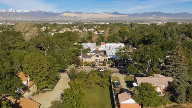 Aerial view of Draper Rehabilitation and Care Center surrounded by trees and residential houses, with mountains visible in the background under a clear sky.