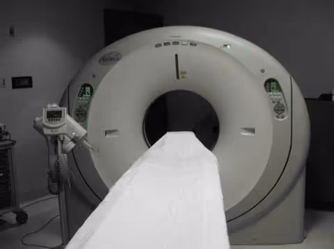 Large medical imaging CT scanner with patient table in a dim hospital room.