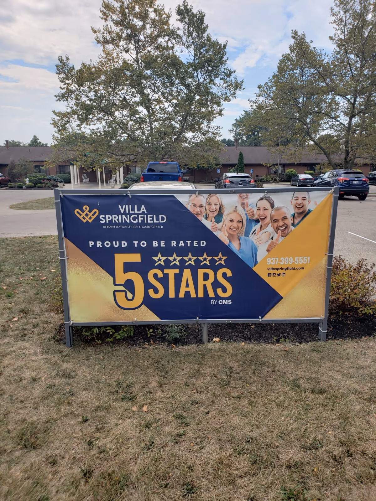 Outdoor banner sign in front of a parking lot and trees, displaying Villa Springfield Rehabilitation & Healthcare Center's 5-star rating by CMS with smiling healthcare staff images and contact information.