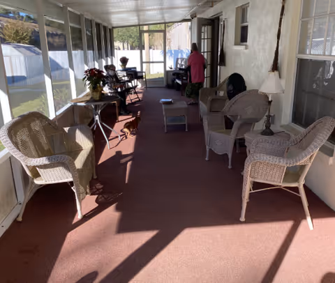 Enclosed sunroom-style seating area with wicker chairs and tables along a carpeted floor and a person standing near the far door.