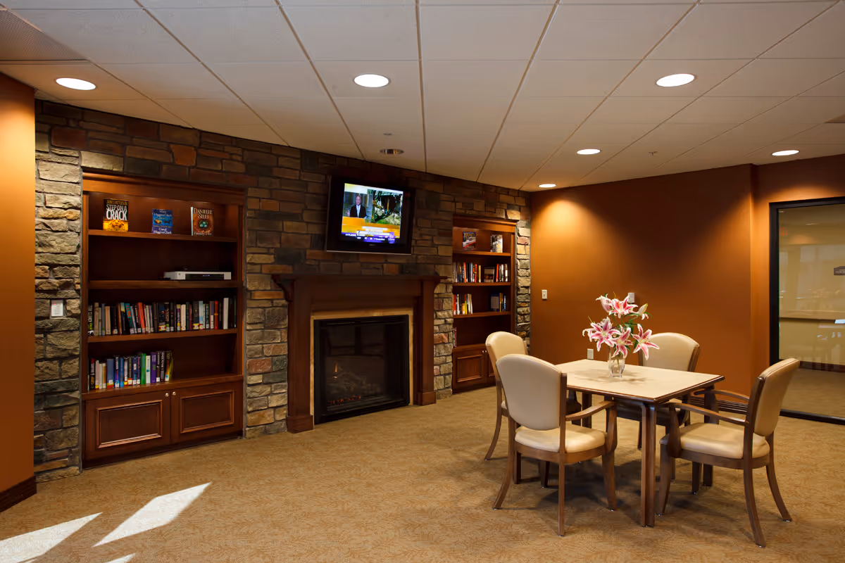 A cozy lounge area featuring a table with chairs, a fireplace, bookshelves, and a television.