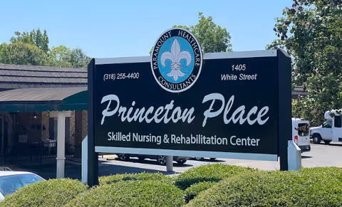 Outdoor sign for Princeton Place Skilled Nursing & Rehabilitation Center located at 1405 White Street, with contact number (318) 255-4400, surrounded by greenery and a parking area in the background.