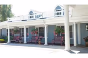 Covered porch with white columns, hanging flower baskets and benches along a light blue building exterior.