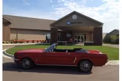 A red vintage convertible parked in front of the main entrance of the Bethany Home Sioux Falls brick building with a covered portico.