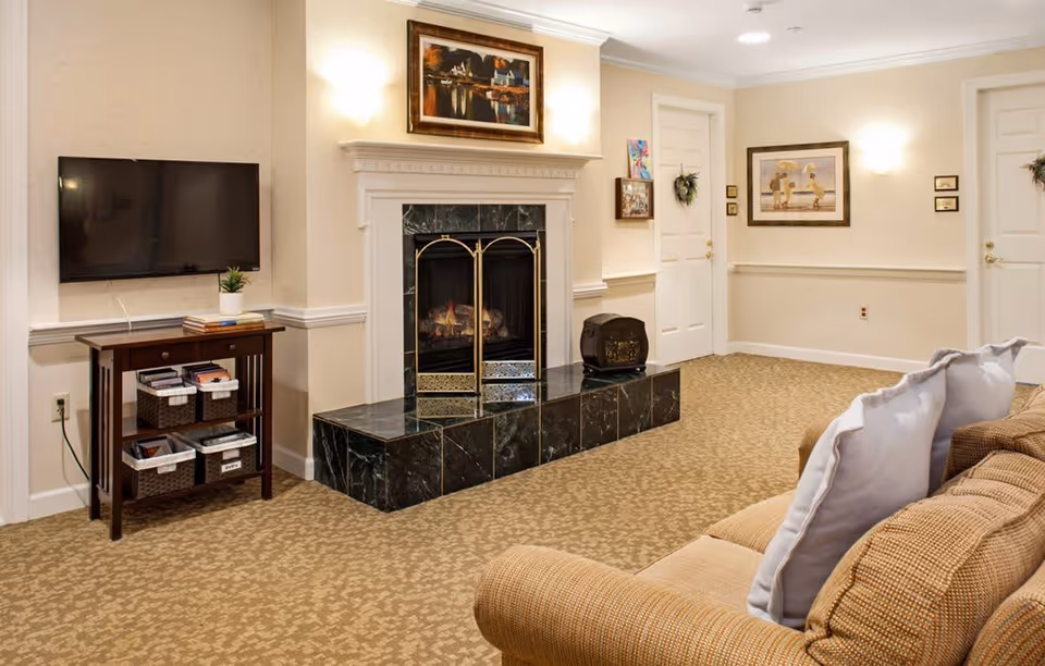 Cozy sitting area with a sofa, wall-mounted TV, marble fireplace, side table with baskets, and framed artwork.