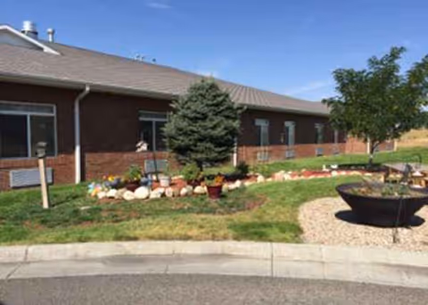 Brick assisted living building with landscaped garden, rocks, tree, and a circular fire pit.