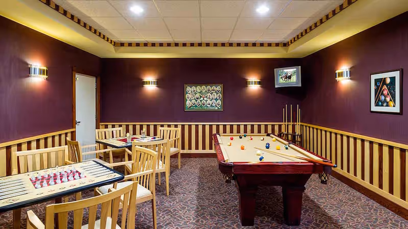 Game room with a pool table, two small game tables with wooden chairs, wall sconces, and framed artwork on purple walls.