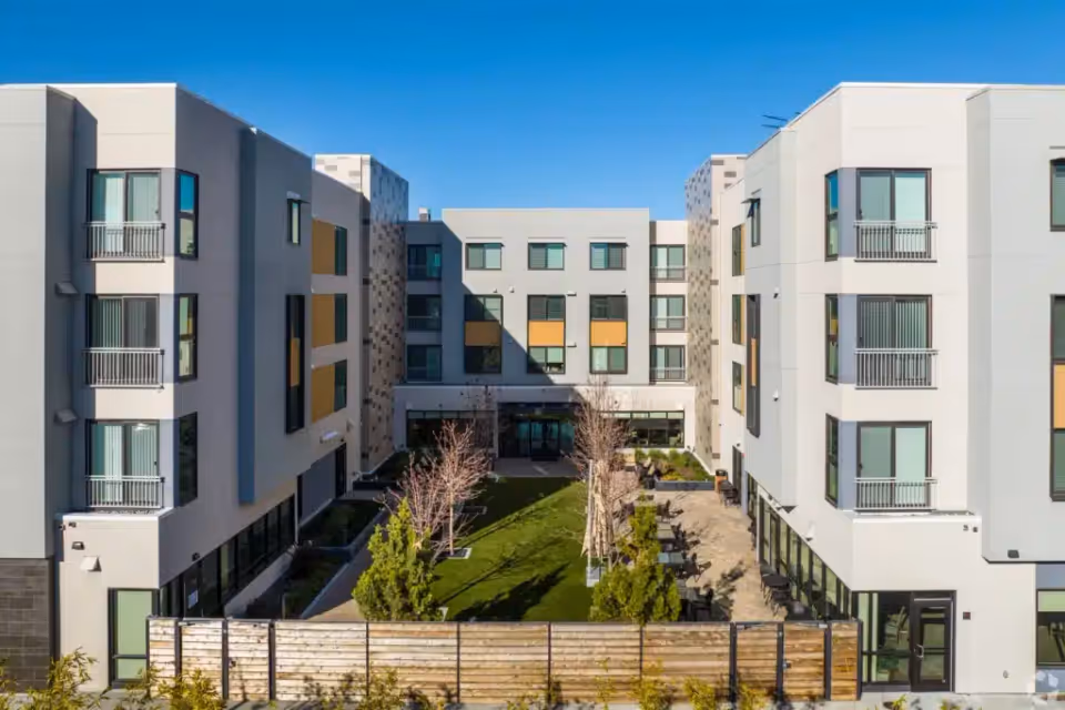 Modern four-story senior living building surrounding a landscaped central courtyard with seating.