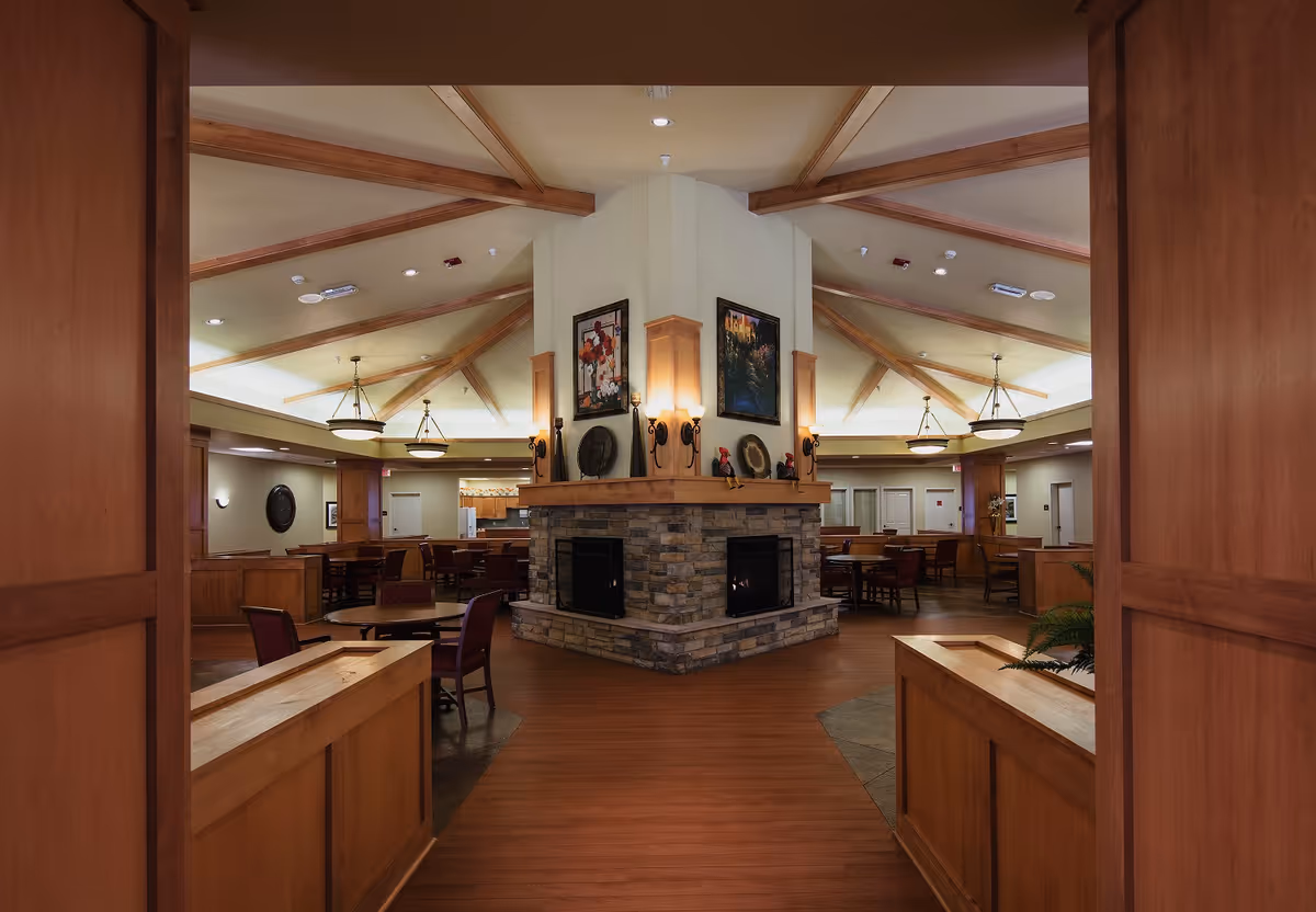 Spacious common dining room with a central stone fireplace, exposed wooden beams, and round dining tables.