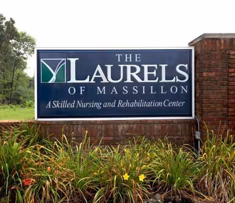 Blue sign reading The Laurels of Massillon beside landscaped plants.