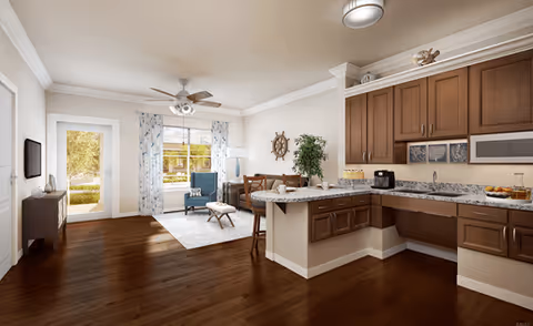 Bright open-plan living area with hardwood floors, a granite-topped kitchen island, and a seating area by a window and glass door.