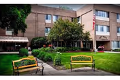Front entrance of Crest Manor Living & Rehab Center with a lawn, benches, trees, and an American flag.