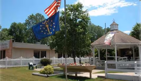 Outdoor area of Miller's Merry Manor with gazebo, flags, white fence, and greenery.