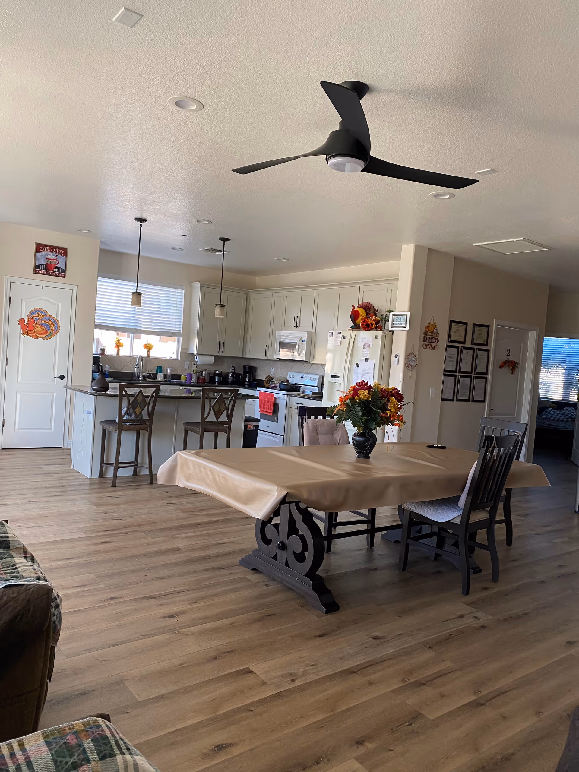Open-plan dining area with a table and vase of flowers in the foreground and a kitchen with an island and barstools in the background.