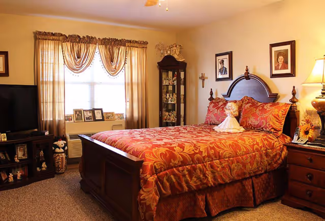Cozy bedroom featuring a wooden bed with red patterned bedding, matching nightstand and dresser, a TV cabinet, and a curtained window.