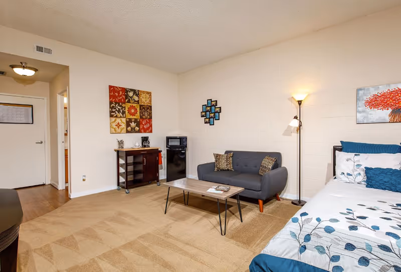 Cozy studio-style living area with a bed, sofa, coffee table, floor lamp, and art.