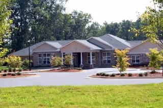 Single-story senior living facility exterior with stone accents, a circular driveway, and landscaped frontage.