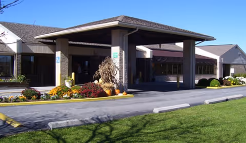 Covered front entrance of a single-story health care facility with a porte-cochère, pumpkins and landscaped flowerbeds.