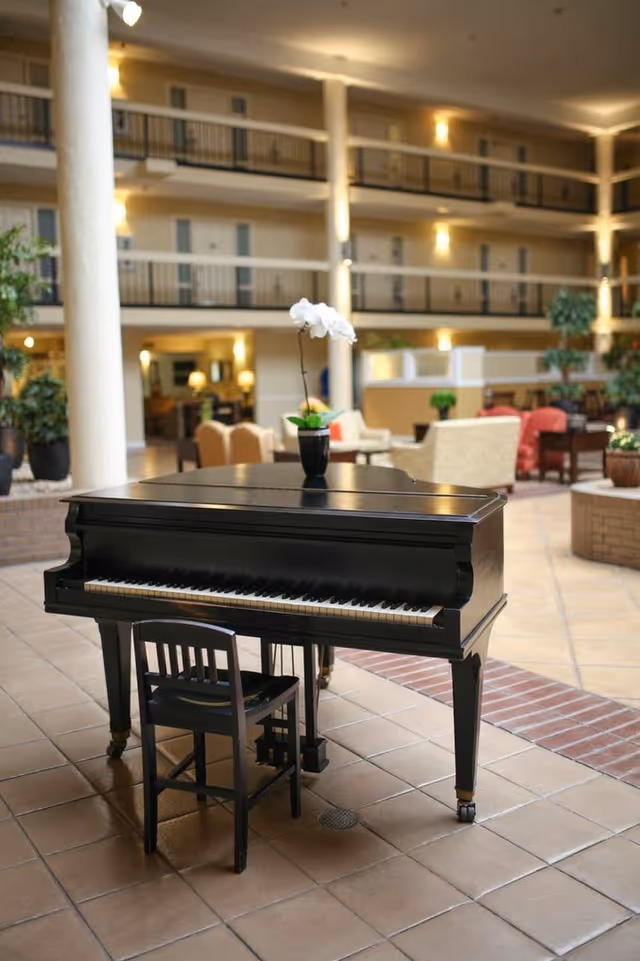 Black grand piano topped with a white orchid in the foreground of a multi-story indoor atrium with seating and balcony walkways.