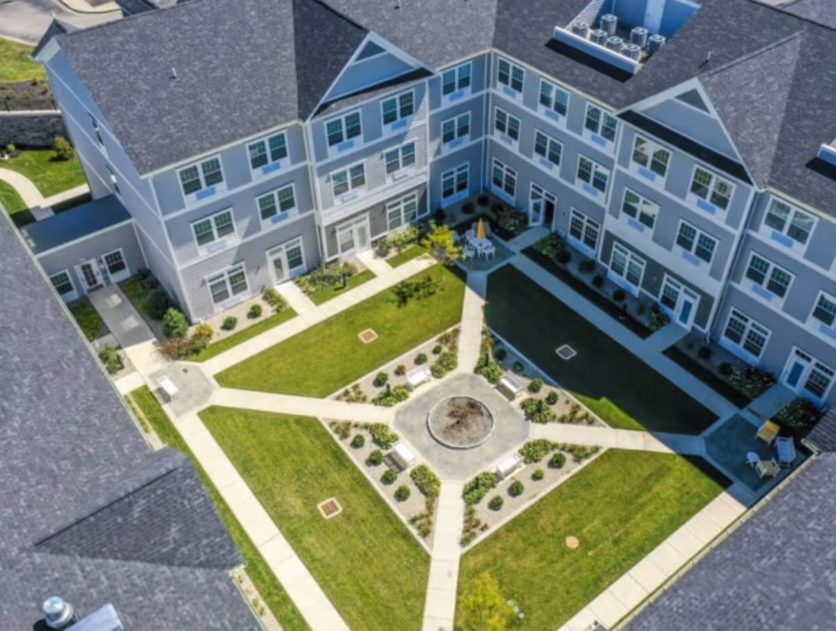 Aerial view of a landscaped central courtyard with intersecting walkways and benches surrounded by a multi-story senior living building.